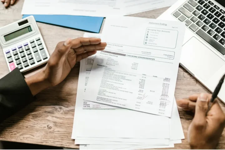 Person reviewing financial documents beside a laptop and calculator
