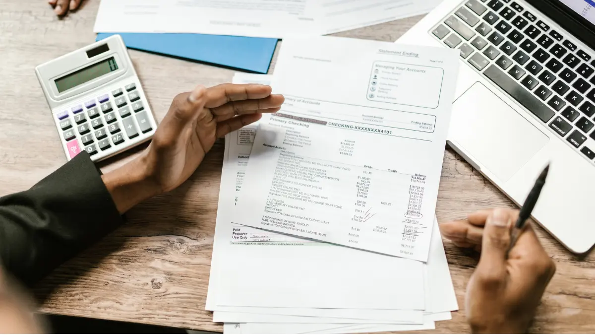 Person reviewing financial documents beside a laptop and calculator